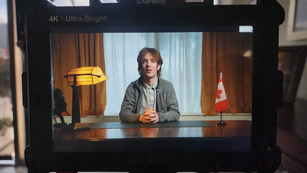 Behind-the-scenes photo of Max, a communications summer student, seated at the desk standing in for MP Corey Hogan during a lighting test in his constituency office, days before the rapid-response shoot.